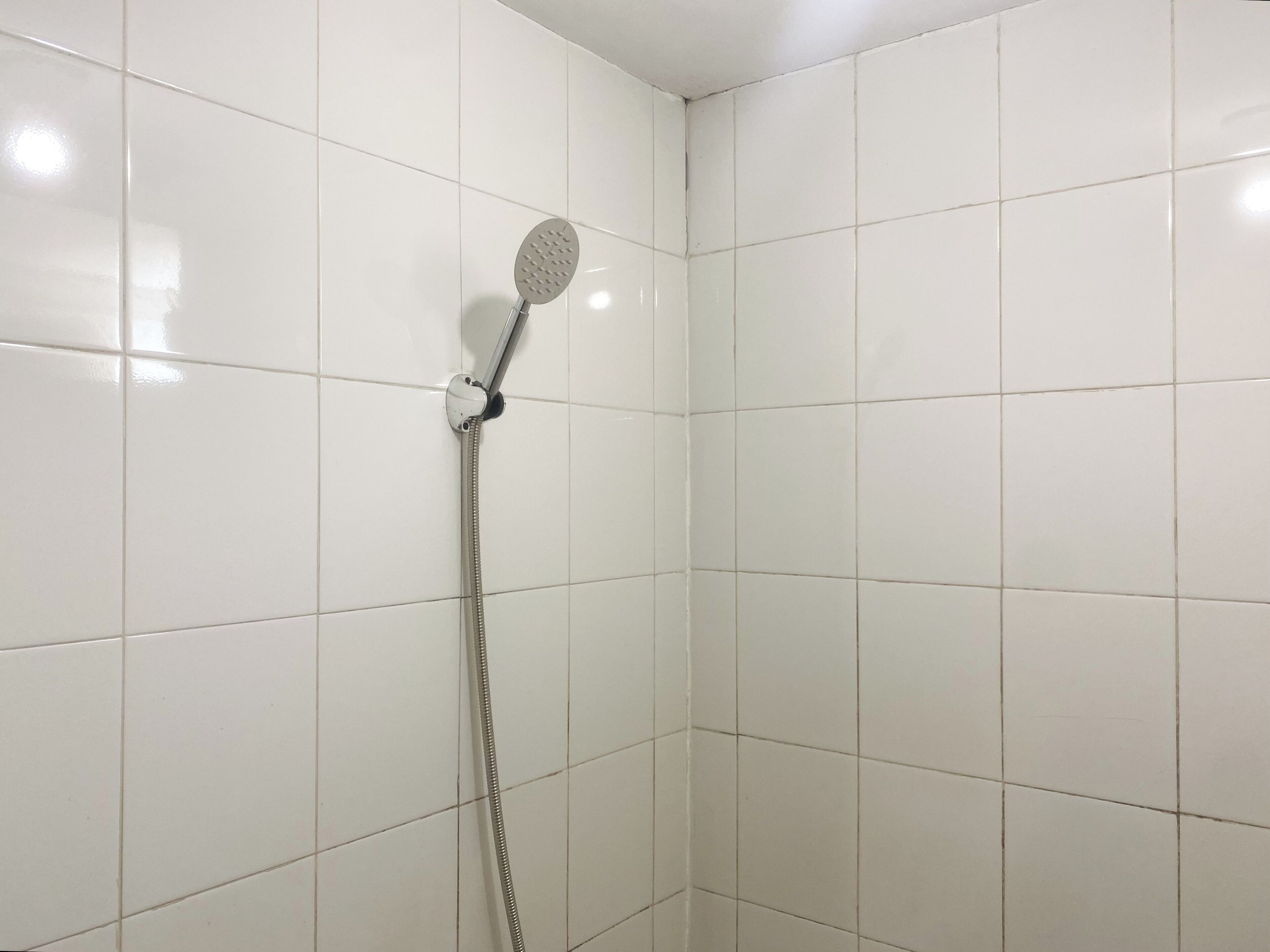 A shower with a handheld showerhead and a flexible hose, set in a room with white tiled walls.