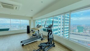 A spacious room with large windows, a treadmill, an elliptical machine, and a set of dumbbells. - Homey And Well Furnished 2Br Grand Kamala Lagoon Apartment (Bekasi)