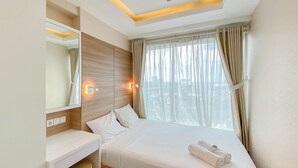 A hotel room with a bed, a desk, a mirror, and a window with curtains. - Homey And Well Furnished 2Br Grand Kamala Lagoon Apartment (Bekasi)