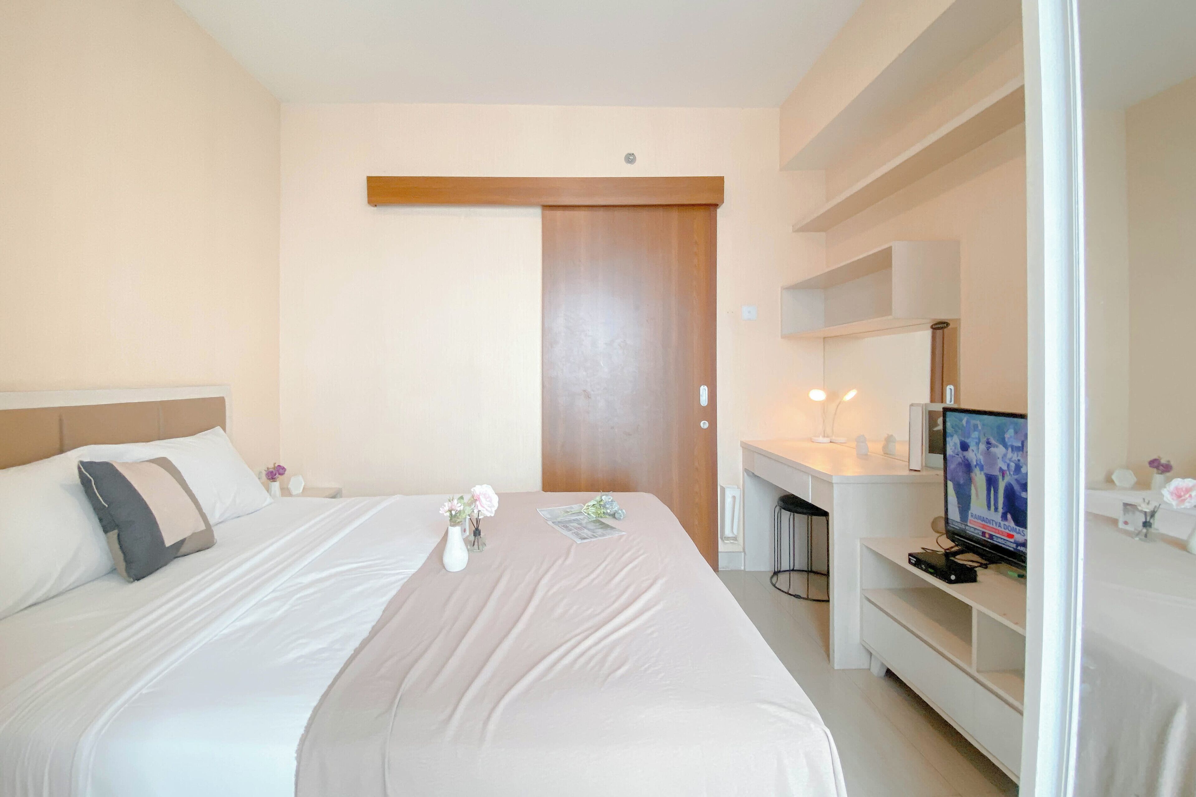 A hotel room with a bed, a desk with a television, and a door.