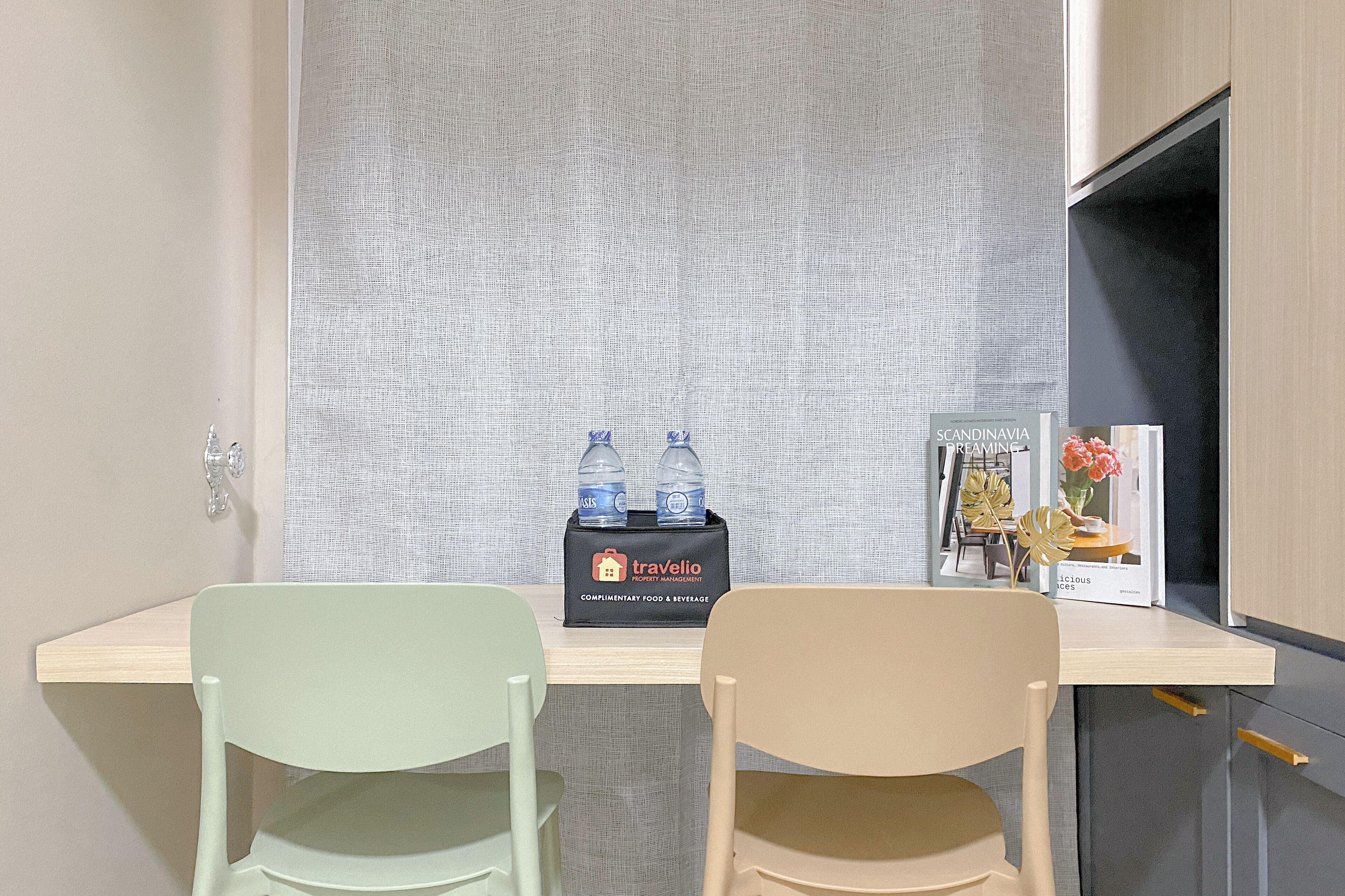 A hotel room with a desk, two chairs, a minibar, and a small table with a vase and a book.