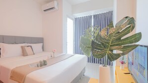 Habitación de hotel con cama, escritorio con computadora, una planta grande y ventana con cortinas.
