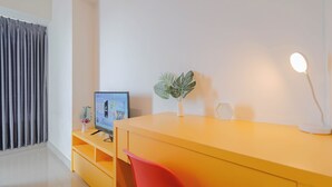 Una sala de estar moderna con un escritorio amarillo, una silla roja, un televisor de pantalla plana, una planta en maceta y una lámpara blanca.