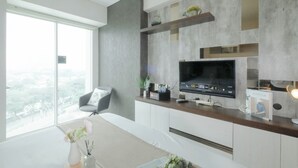 A modern living room with a large window, a flat-screen TV, and a minimalist design. - Cozy And Good Studio At Grand Kamala Lagoon Apartment (Bekasi)