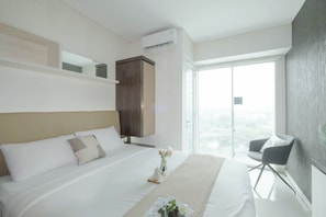 Una habitación de hotel moderna con una cama grande, un armario de madera, un sillón pequeño y un puerta de cristal corredera que da a un balcón.