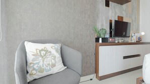 A modern living room with a grey sofa, a white cabinet with a TV, and a small plant. - Cozy And Good Studio At Grand Kamala Lagoon Apartment (Bekasi)