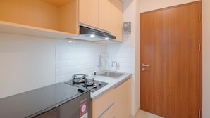 A compact kitchen with a black countertop, a built-in stove, a double sink, and wooden cabinets. - Serene Living Studio Apartment Grand Kamala Lagoon (Bekasi)