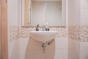 A bathroom with a white sink, a mirror above it, and a tiled backsplash. - Comfy And Elegant 2Br At Tamansari Iswara Apartment (Bekasi)