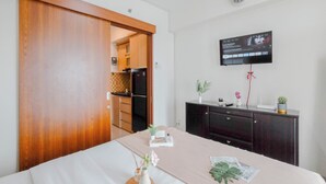 Une chambre d’hôtel avec un lit, un téléviseur fixé au mur, une armoire en bois et, au fond, une petite kitchenette.