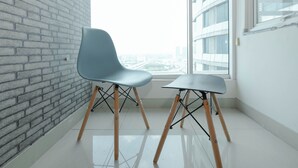 A modern room with a brick wall, two chairs with wooden legs, and a large window with a city view. - Studio Near Gunadarma University Bekasi At Grand Kamala Lagoon Apartment (Bekasi)