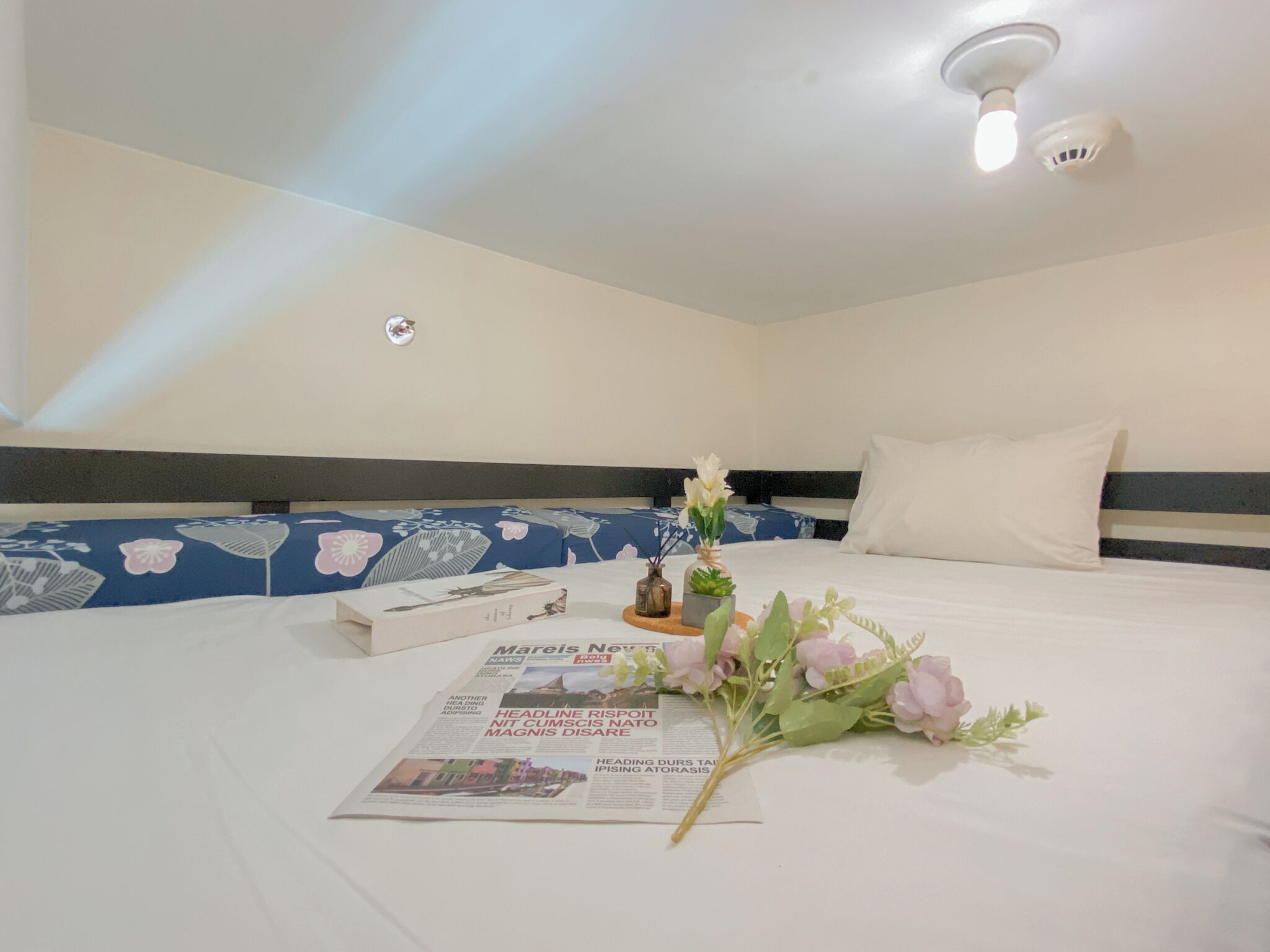 Une chambre d’hôtel avec un lit soigneusement fait, un bouquet de fleurs et un journal posé sur le lit.