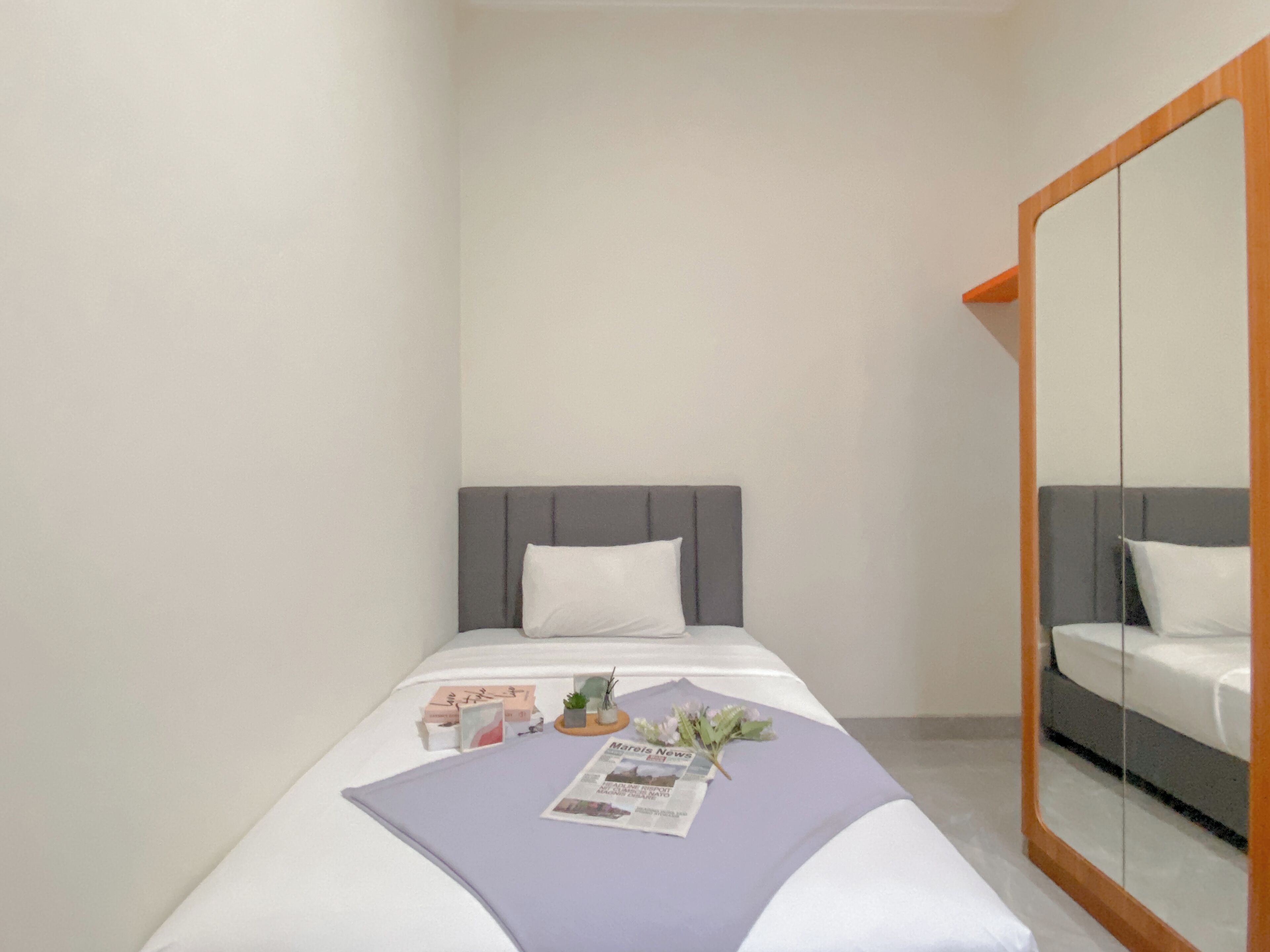 A hotel room with a bed, a large mirror, and a small table with a newspaper and flowers.