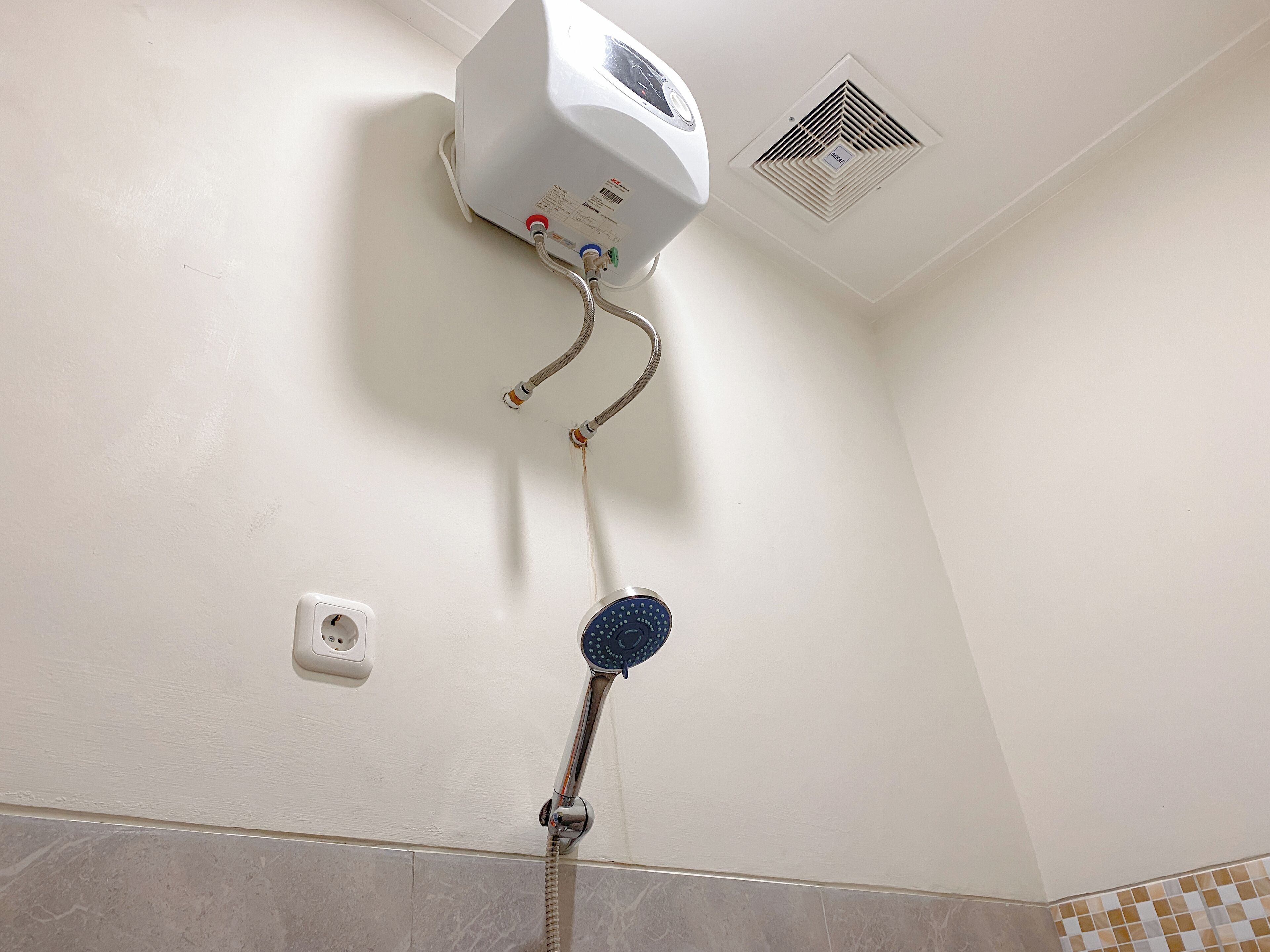 A bathroom with a wall-mounted shower, a ceiling vent, and a power outlet.