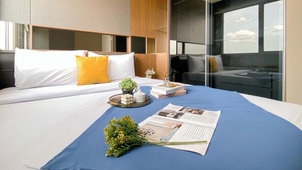 Ein modernes Hotelzimmer mit einem großen Bett, einem Nachttisch mit Pflanze, einem Tablett mit Dekoration und einer Zeitschrift.