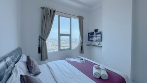 A hotel room with a large bed, a TV mounted on the wall, and a window with curtains. - Chic And Sleek Studio At The City Square Surabaya Apartment (Surabaya)