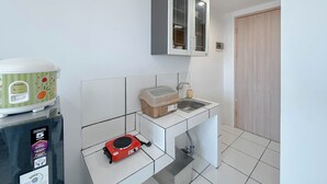A compact kitchen with a refrigerator, a washing machine, a red appliance, a sink, and a cabinet. - Chic And Sleek Studio At The City Square Surabaya Apartment (Surabaya)