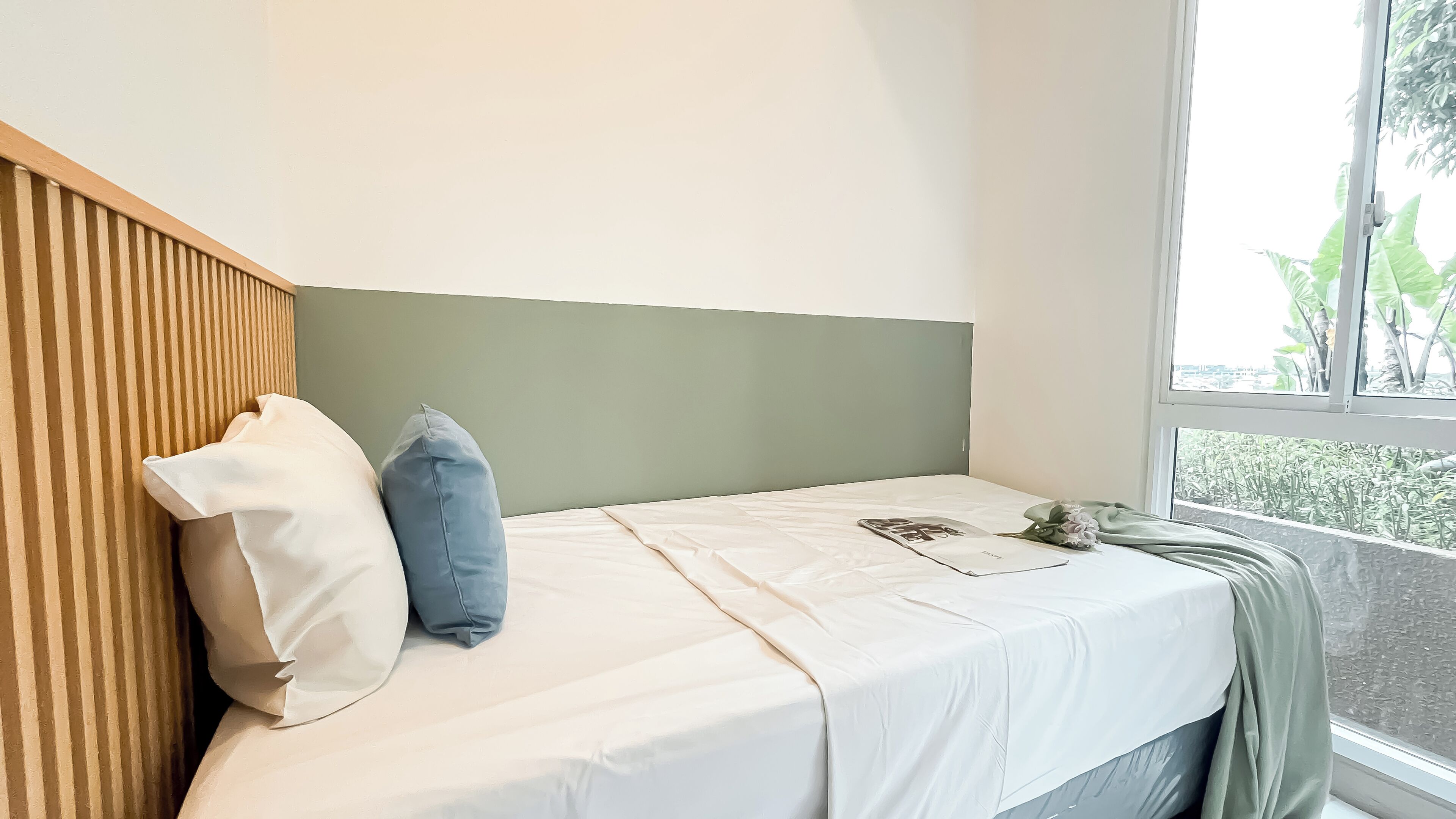 A neatly made bed with a striped headboard, a window with a view of greenery, and a single pillow.