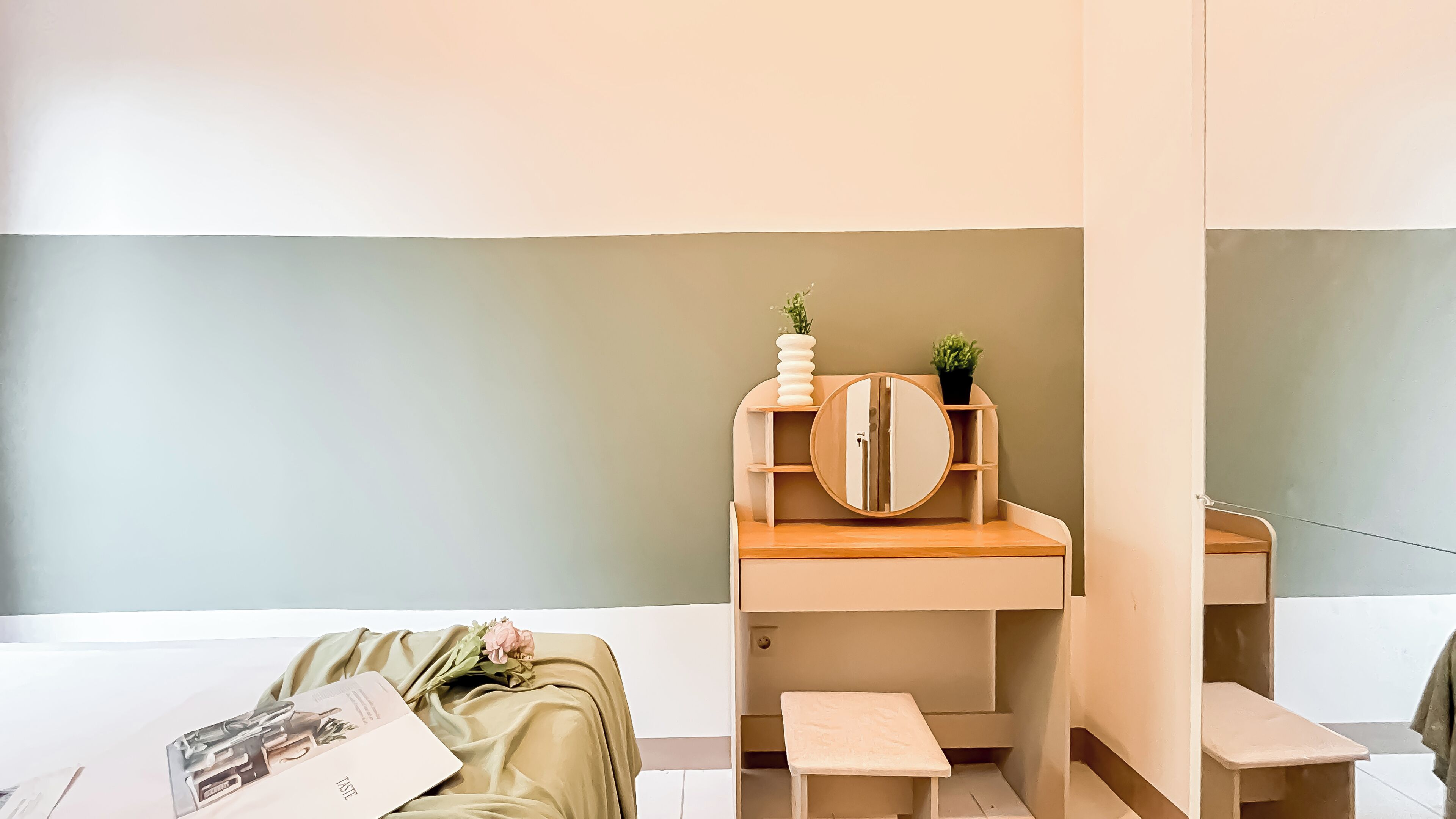 Una camera da letto minimalista con una toeletta in legno, uno sgabello piccolo e un letto con coperta verde.