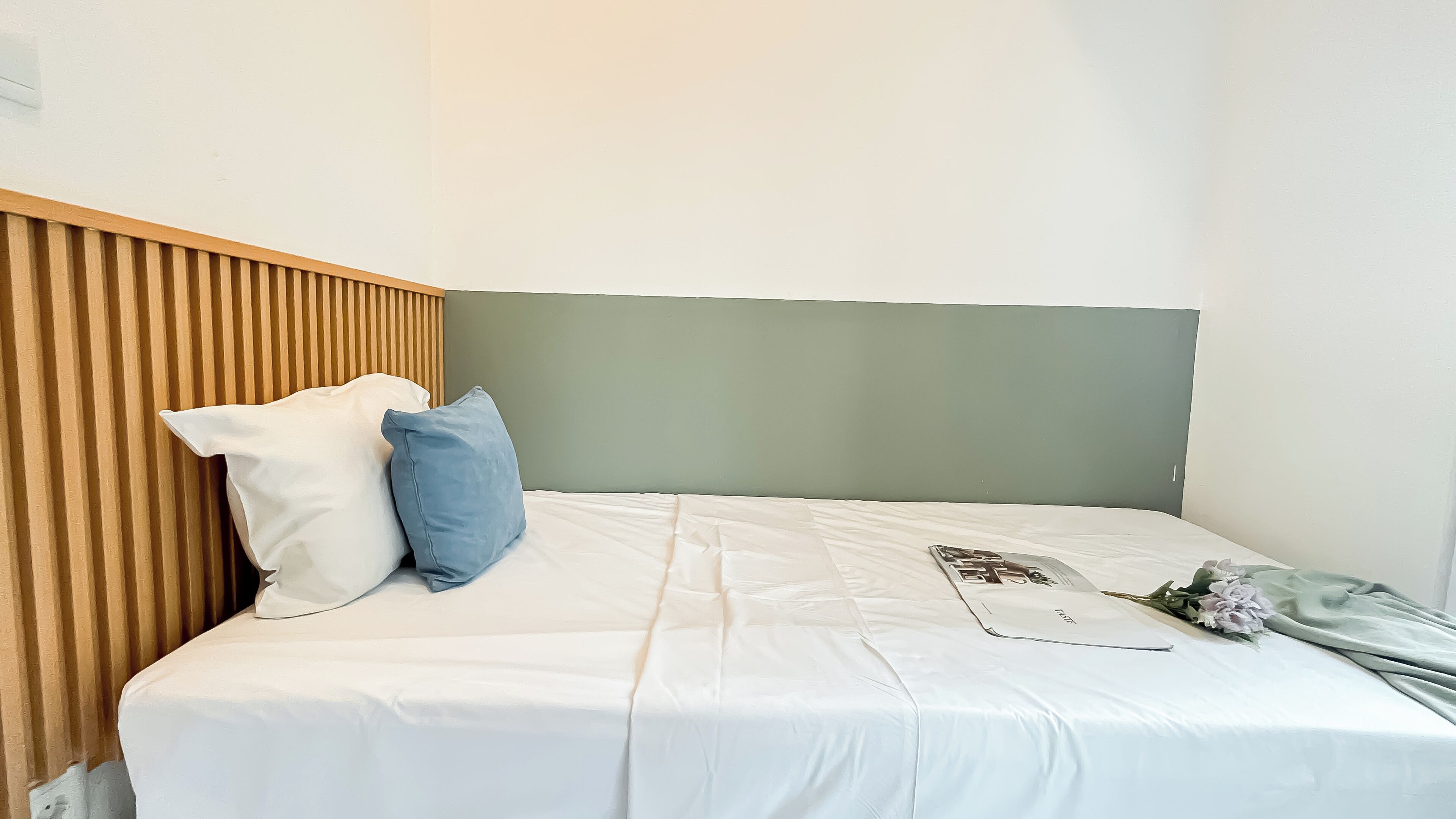 A neatly made bed with white bedding and two pillows, a wooden headboard, and a green wall.