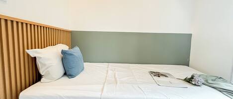 A neatly made bed with white bedding and two pillows, a wooden headboard, and a green wall.
