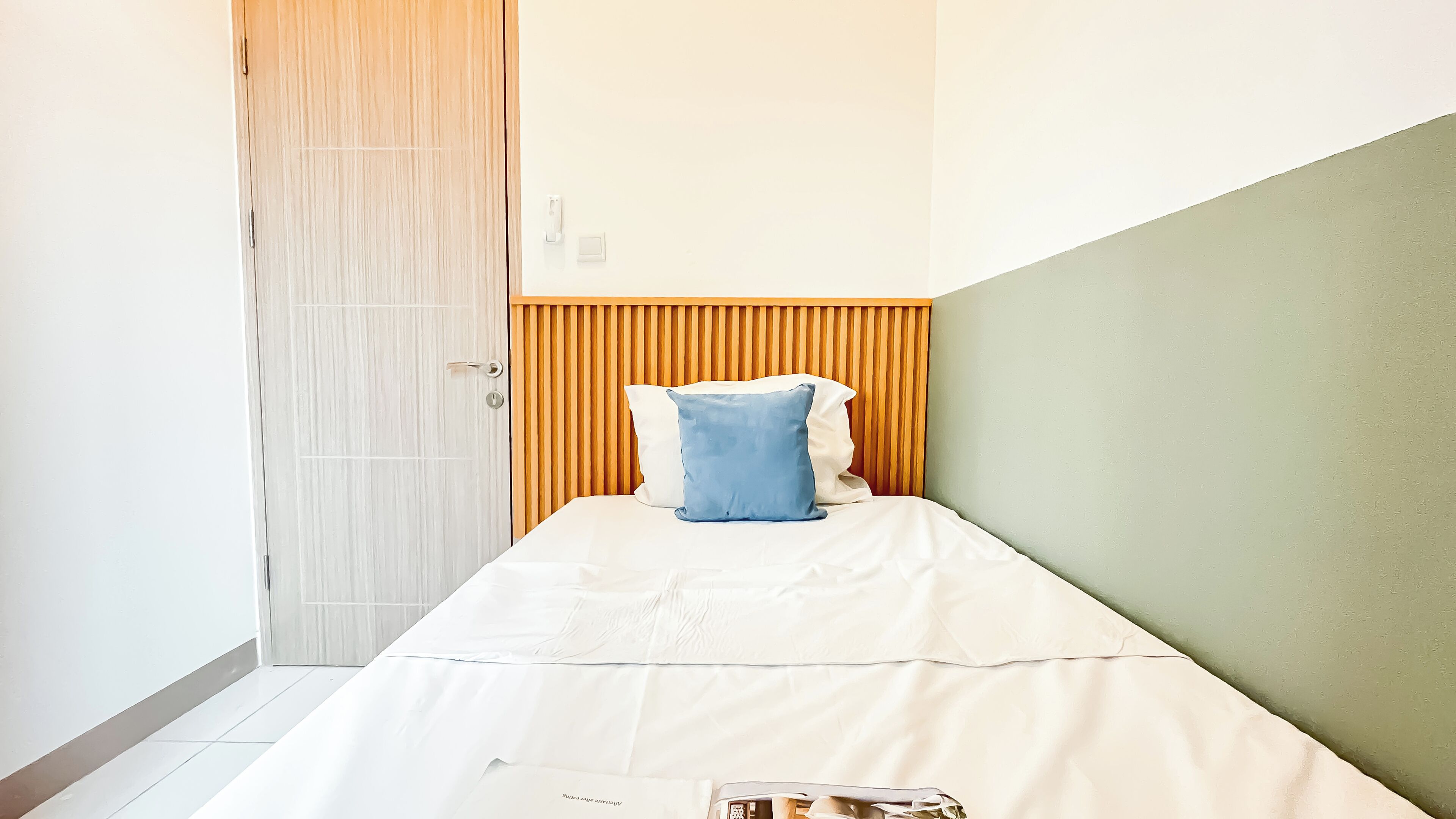 A small, neatly arranged bedroom with a single bed, a wooden headboard, and a white door.
