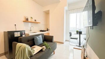 Una sala de estar moderna con un sofá gris, una mesita y una zona de cocina con un lavamanos y una encimera.