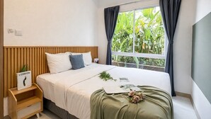 A bedroom with a bed, a nightstand, a window with curtains, and a view of greenery outside. - Contemporary And Cozy 2Br At Apartment Tokyo Riverside Pik 2 (Teluknaga)