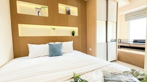 A modern bedroom with a large bed, a headboard with built-in shelves, and a view of a balcony. - Warm And Comfy 2Br At Green Bay Pluit Apartment (Jakarta)