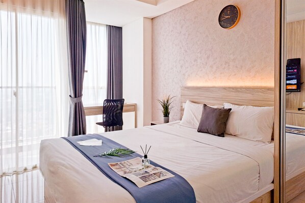A hotel room with a large bed, a clock on the wall, and a VITA card reader on the nightstand. - Delightfully Cozy Studio Apartment Pacific Garden - Campus Town @Alam Sutera (Tangerang)