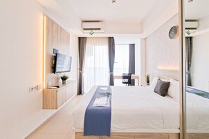 Et hotelværelse med seng, sengebord, fjernsyn, aircondition og et vindue med gardiner.