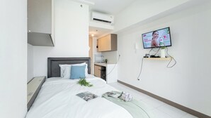 Moderni hotellihuone, jossa on sänky, seinälle asennettu televisio ja pieni keittotila.