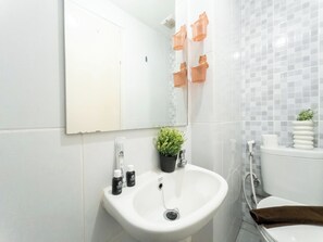 A bathroom with a white sink, a mirror, a potted plant, and a toilet. - Comfy And Neat Studio At Tokyo Riverside Pik 2 Apartment Near Tokyo Hub (Teluknaga)