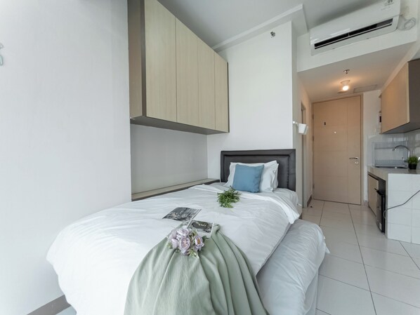 A modern bedroom with a bed, a small bedside table, a nightstand, a built-in wardrobe, and a kitchenette with a sink and countertop. - Comfy And Neat Studio At Tokyo Riverside Pik 2 Apartment Near Tokyo Hub (Teluknaga)