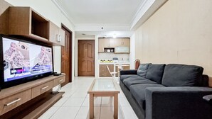 Ein Wohnzimmer mit Fernseher, einer Couch, einem Couchtisch und einer Küchenzeile im Hintergrund.