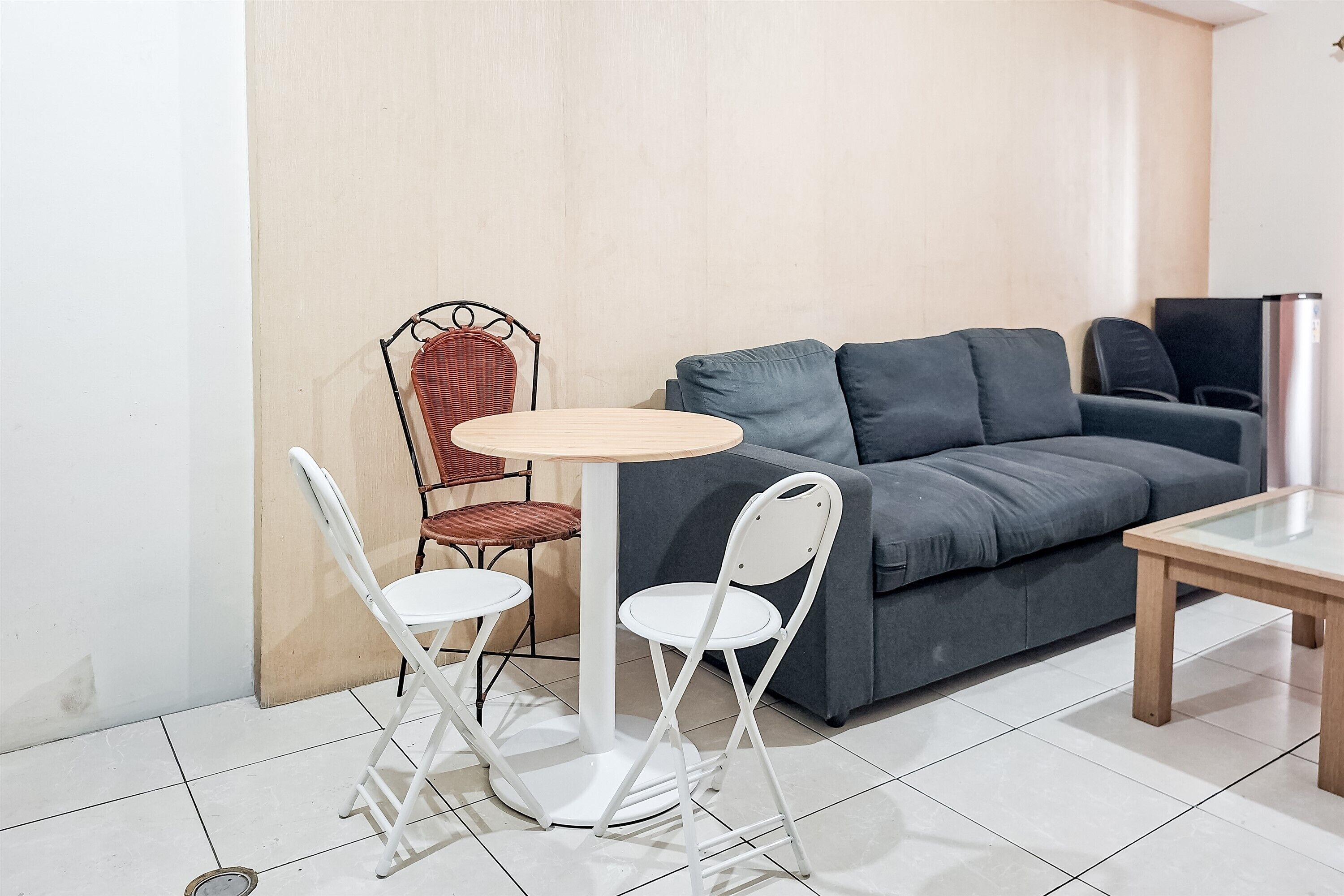 Una sala moderna con un sofá gris, una mesita redonda y dos sillas blancas.