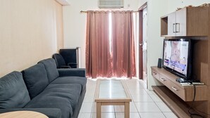Ein Wohnzimmer mit einem dunkelgrauen Sofa, einem kleinen Holztisch, einem Fernseher auf einem Holzschrank und einer Schiebetür mit Vorhang.