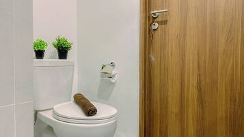 Une salle de bain avec des toilettes, une porte en bois et deux plantes en pot posées sur une étagère.