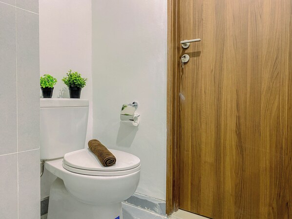 Un bagno con un water, una porta in legno e due piante in vasi su uno scaffale.