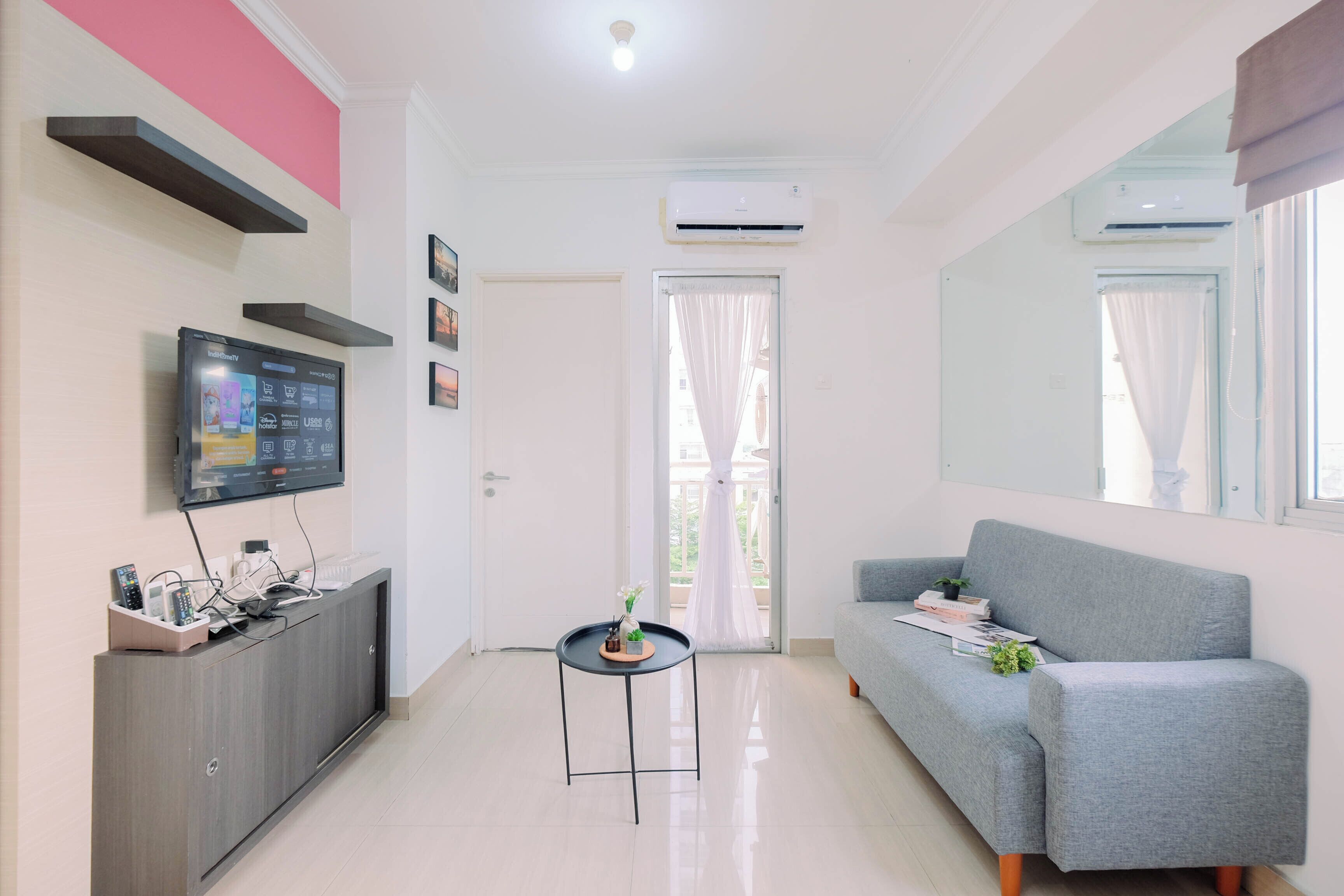 A modern living room with a grey sofa, a TV mounted on a cabinet, and a small table with a plant.