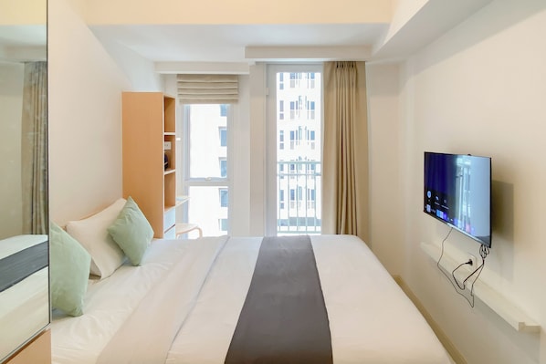 A hotel room with a bed, a TV mounted on the wall, a wardrobe, and a window with curtains. - Restful Living Studio At Apartment Tokyo Riverside Pik 2 (Teluknaga)