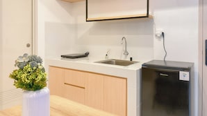 A modern kitchen with white tiles, a sink, a black refrigerator, and a wooden cabinet. - Lovely And Pleasant 2Br Apartment At Tokyo Riverside Pik 2 (Teluknaga)