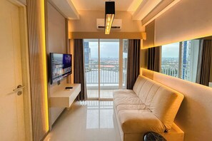 A modern living room with a large window, a flat-screen TV, and a sofa. - Contemporary Cozy 2Br With Direct Access To Mall At Tanglin Supermall Mansion Apartment (Surabaya)