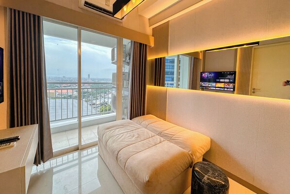 A modern hotel room with a large bed, a TV on the wall, and a view of the city through the window. - Contemporary Cozy 2Br With Direct Access To Mall At Tanglin Supermall Mansion Apartment (Surabaya)