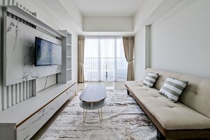 A modern living room with a sofa, a flat-screen TV mounted on a marble wall, and a coffee table. - 2Br Near British School Jakarta At Tamansari Bintaro Mansion Apartment (South Tangerang)