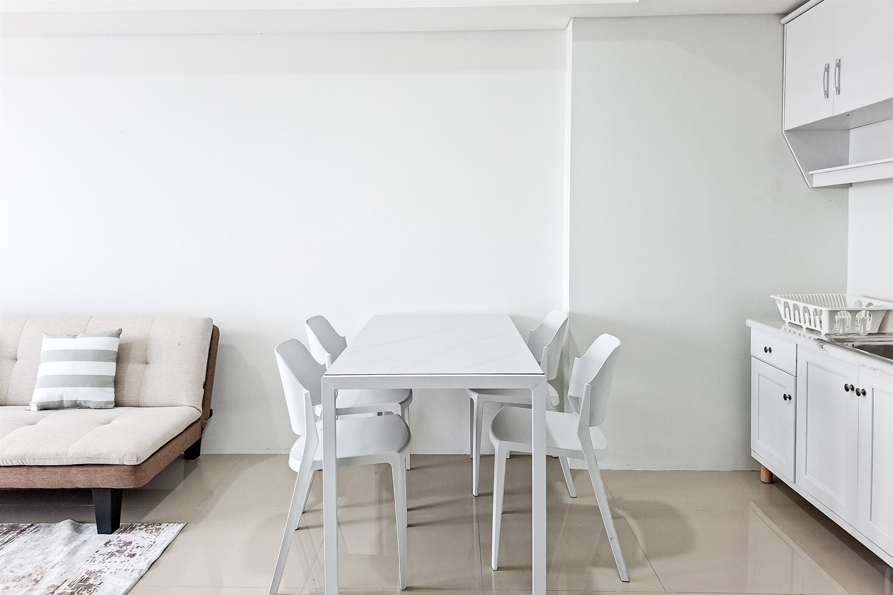 A modern, minimalist room with a white sofa, a white dining table with chairs, and white cabinetry.