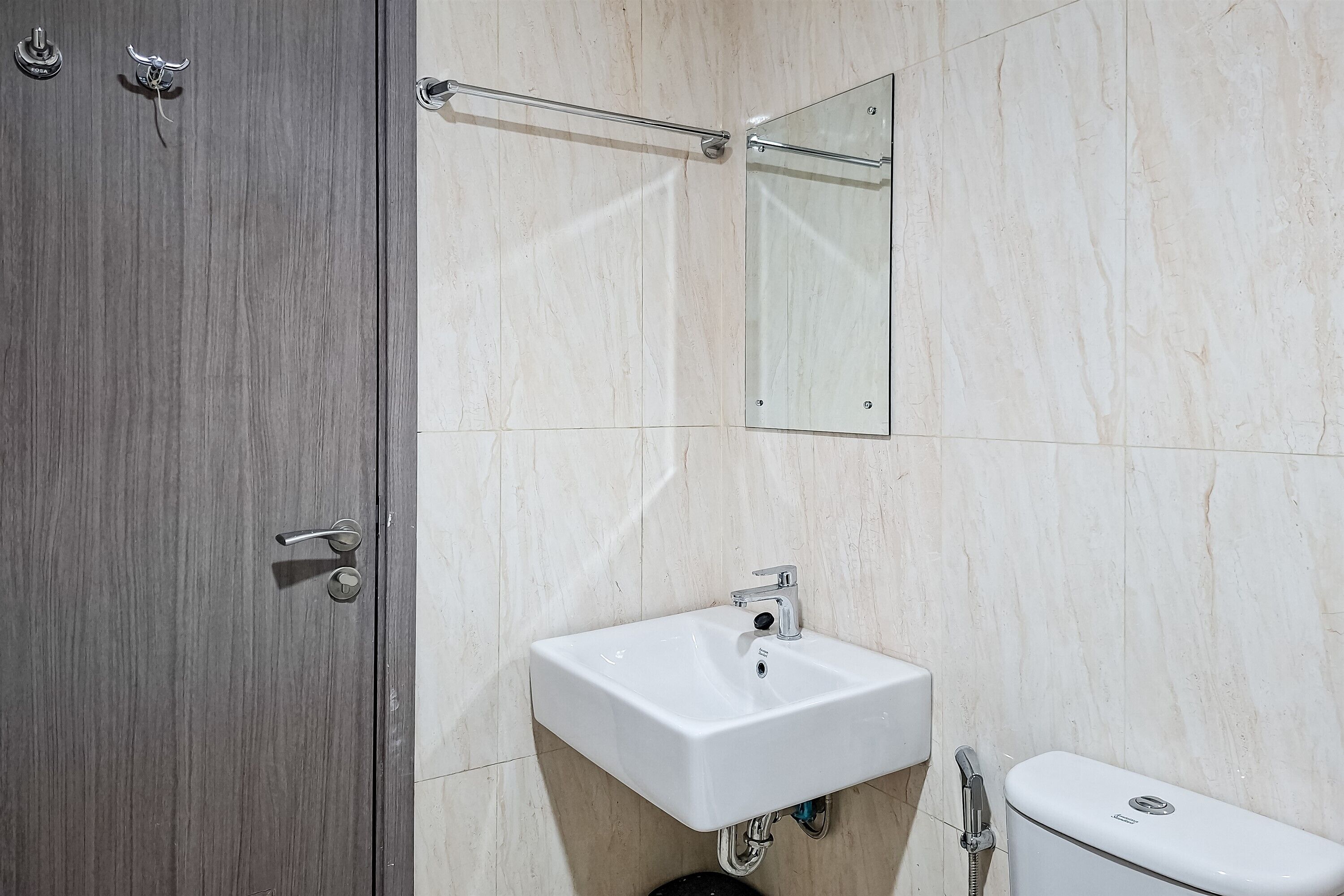 Un baño con puerta de madera, lavamanos blanco, espejo y retrete.
