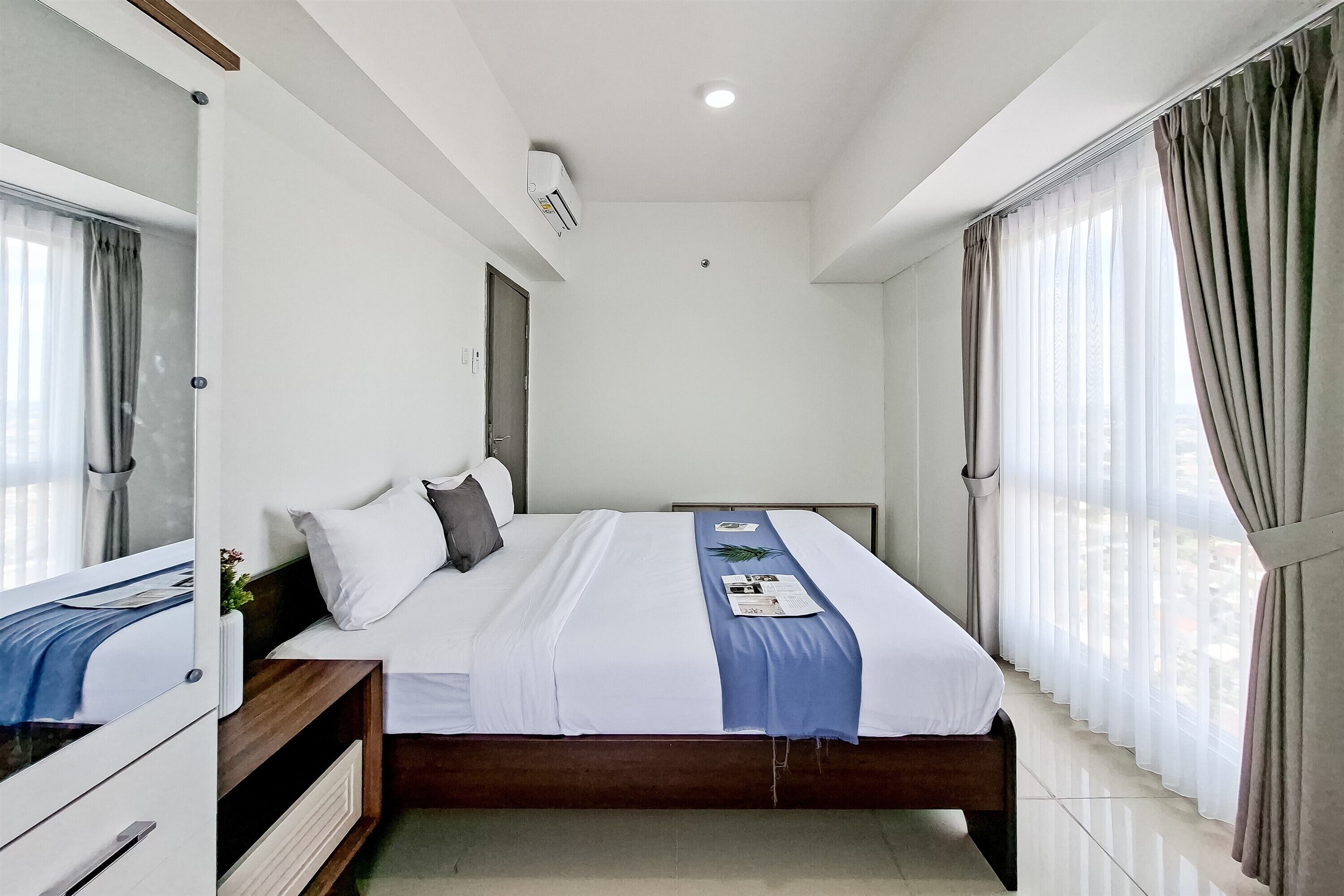 Ein Hotelzimmer mit Bett, Nachttisch, Spiegel und einem Fenster mit Vorhängen.
