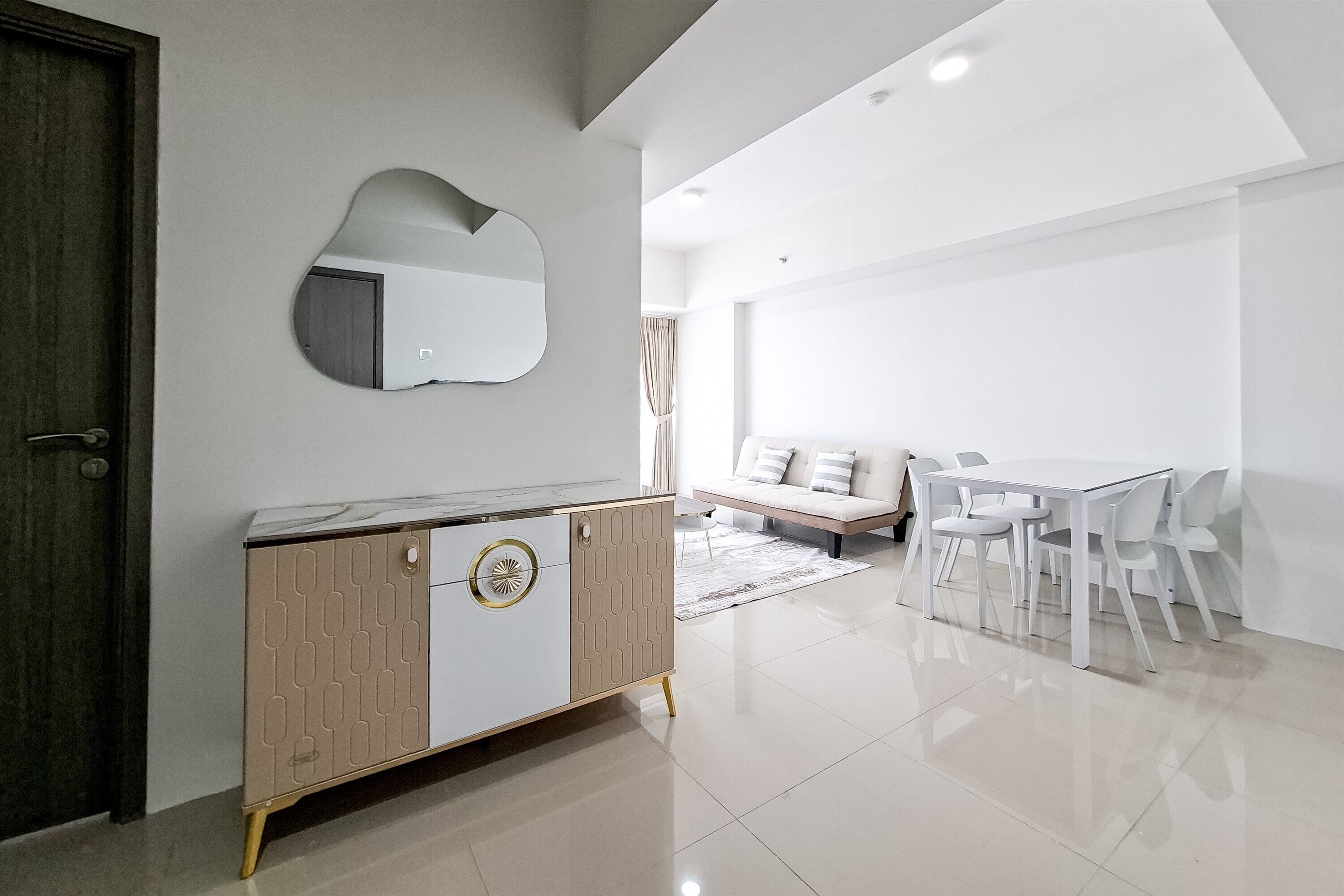 A modern living room with a white sofa, a dining table with chairs, and a wooden cabinet with a mirror.