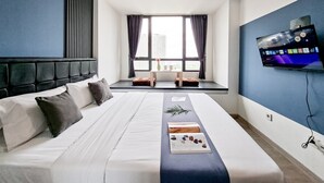 A modern hotel room with a large bed, a TV mounted on the wall, and a window with curtains. - Blue Studio At Apartment Collins Boulevard (Tangerang)