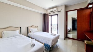 A hotel room with two beds, a wooden desk, a mirror, and a sliding door to a balcony. - Classic Studio At Atria Residence Gading Serpong Apartment (Gading Serpong)
